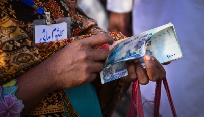 A female road maintenance worker in Pakistan counting her salary during a cash distribution at a mobile service vehicle of Tameer Bank